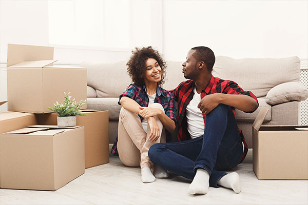 A homeowner couple sitting on the living room floor surrounded by moving boxes